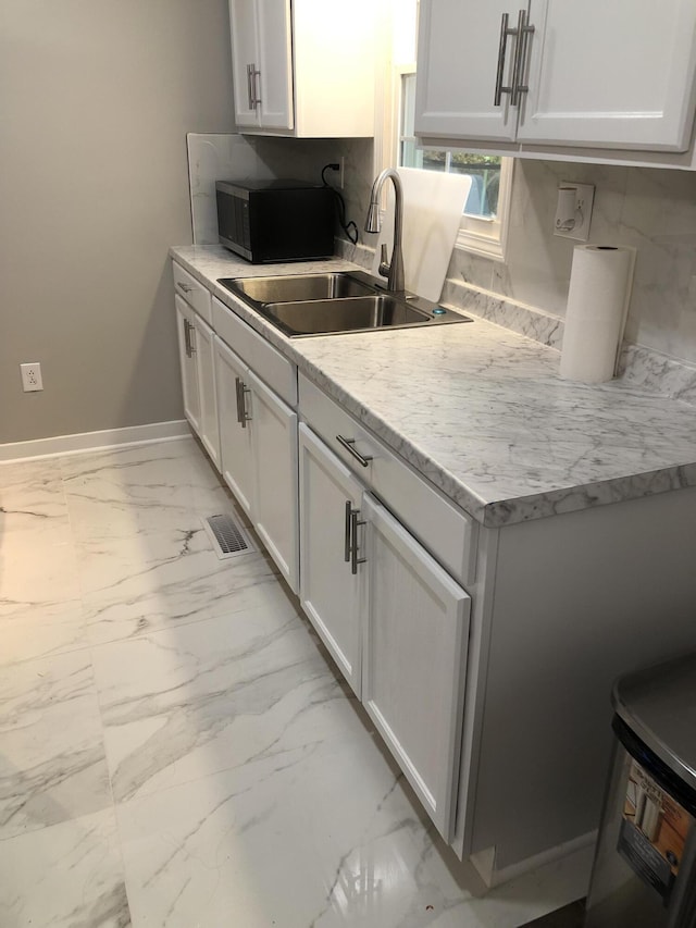 kitchen with white cabinets, light stone counters, and sink