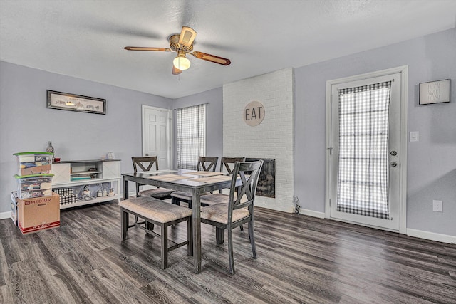 dining area with a textured ceiling, ceiling fan, dark hardwood / wood-style floors, and a brick fireplace