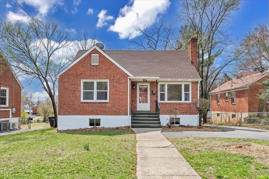 bungalow-style home featuring fence, a front yard, a shingled roof, brick siding, and a chimney