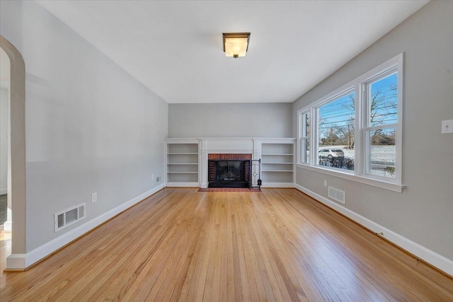 unfurnished living room with light hardwood / wood-style floors and a brick fireplace