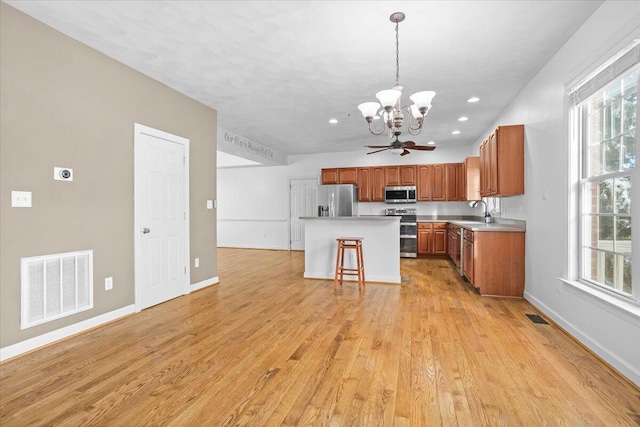 kitchen featuring a center island, hanging light fixtures, appliances with stainless steel finishes, a kitchen breakfast bar, and light hardwood / wood-style floors