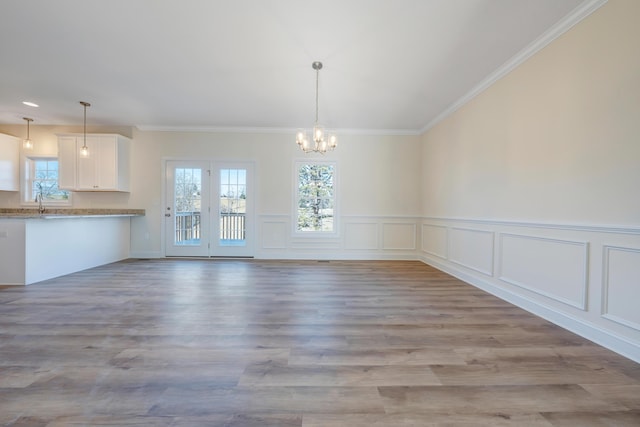 unfurnished dining area with sink, ornamental molding, a chandelier, and light hardwood / wood-style floors