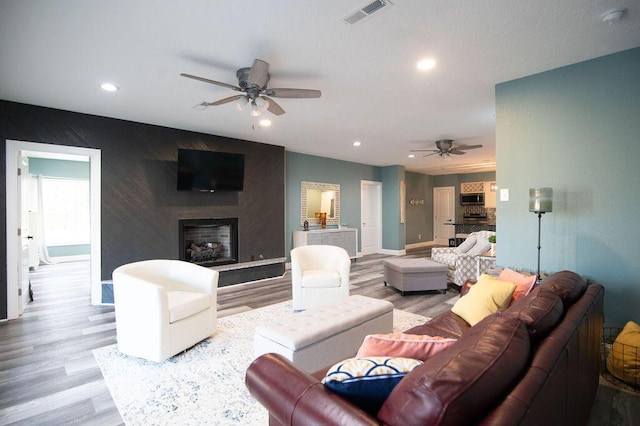 living room with ceiling fan, a fireplace, and light hardwood / wood-style flooring