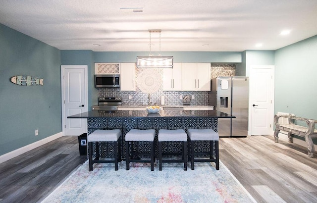 kitchen featuring a kitchen bar, hardwood / wood-style floors, stainless steel appliances, and white cabinetry