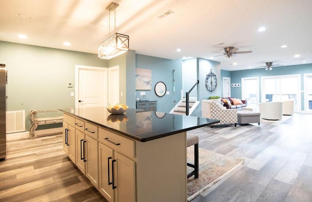 kitchen featuring ceiling fan, pendant lighting, a kitchen bar, a kitchen island, and light wood-type flooring