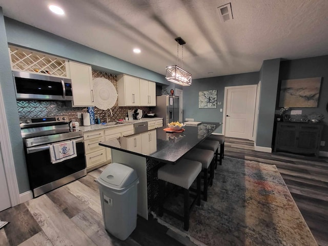 kitchen featuring decorative backsplash, appliances with stainless steel finishes, pendant lighting, and hardwood / wood-style floors