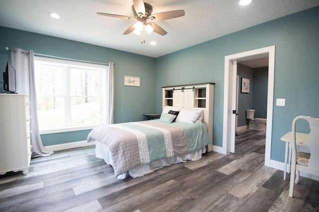 bedroom with a textured ceiling, hardwood / wood-style flooring, ceiling fan, and a barn door