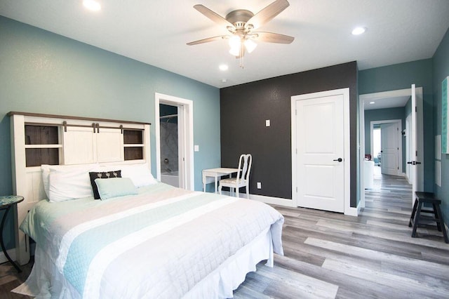 bedroom featuring a barn door, ceiling fan, and wood-type flooring