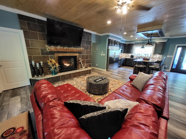 living room with ornamental molding, ceiling fan, wooden ceiling, hardwood / wood-style floors, and a tiled fireplace