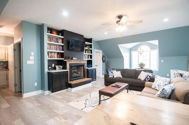 living room featuring lofted ceiling, ceiling fan, built in shelves, a textured ceiling, and light hardwood / wood-style floors