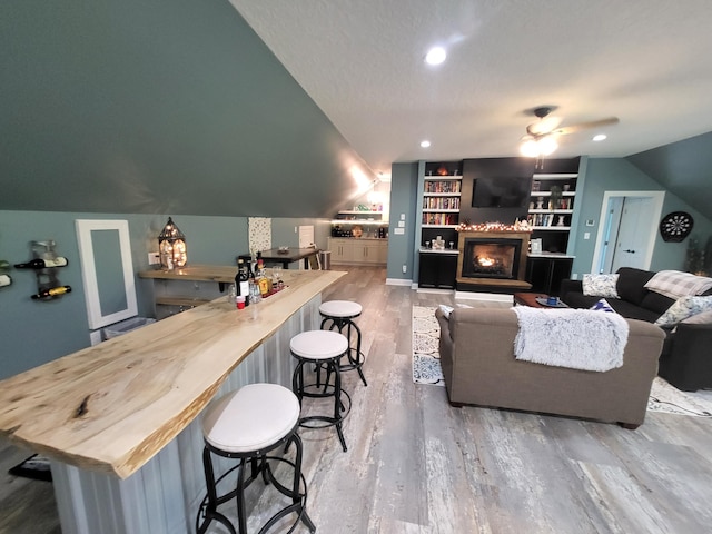 living room with a textured ceiling, hardwood / wood-style flooring, built in features, and lofted ceiling