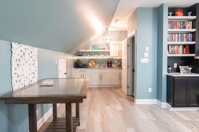 dining room with built in shelves, light hardwood / wood-style flooring, and lofted ceiling