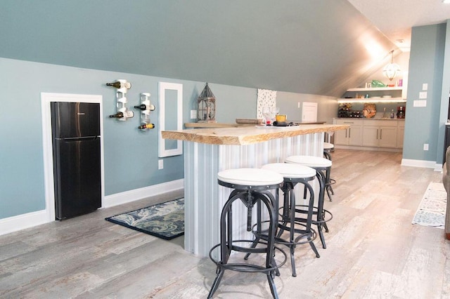 bar featuring wooden counters, black fridge, vaulted ceiling, light hardwood / wood-style flooring, and white cabinetry