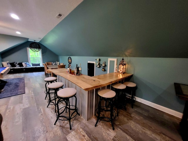 bar featuring wood-type flooring, vaulted ceiling, and butcher block counters