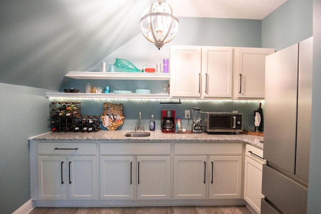 kitchen with sink, light stone countertops, fridge, decorative light fixtures, and white cabinetry