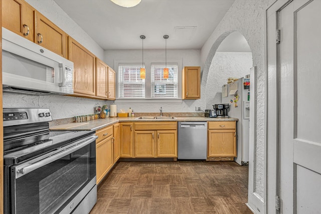 kitchen with stainless steel appliances, light brown cabinetry, sink, and hanging light fixtures