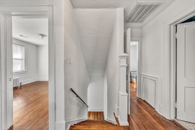 stairway featuring hardwood / wood-style floors, radiator heating unit, and a textured ceiling