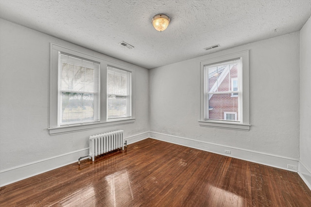 empty room with radiator, dark wood-type flooring, and plenty of natural light