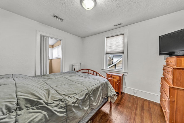 bedroom with dark hardwood / wood-style floors, radiator, and a textured ceiling