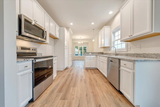 kitchen featuring pendant lighting, white cabinets, light hardwood / wood-style floors, light stone counters, and stainless steel appliances