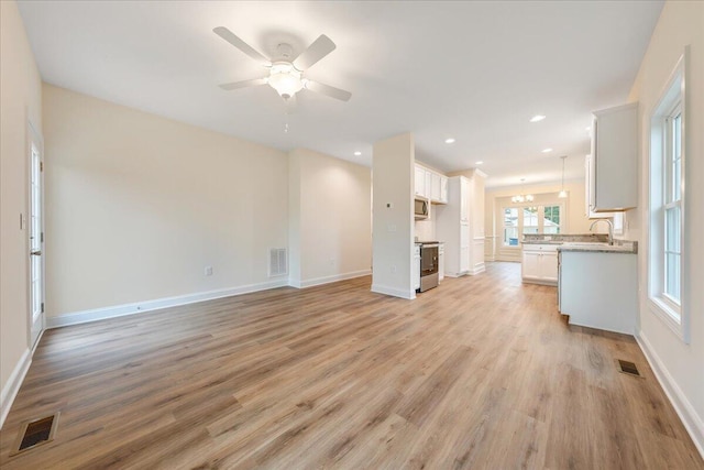 unfurnished living room with ceiling fan with notable chandelier, sink, and light hardwood / wood-style flooring