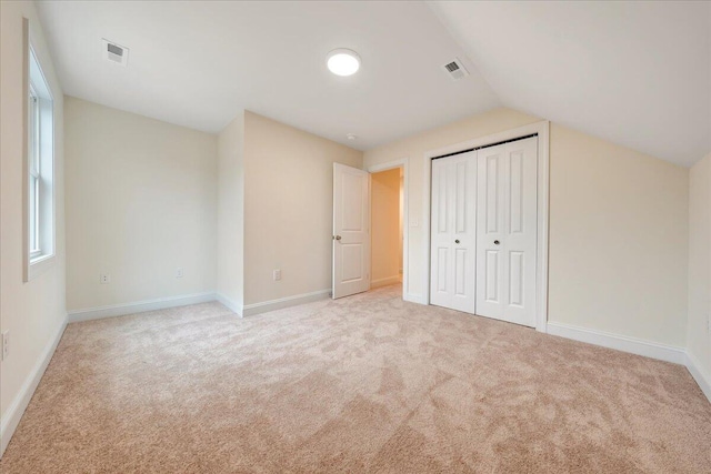 unfurnished bedroom featuring light carpet, a closet, and lofted ceiling