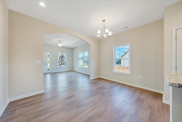 empty room featuring ceiling fan with notable chandelier and light wood-type flooring