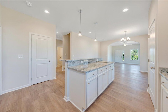 kitchen with light stone countertops, a center island, light hardwood / wood-style flooring, pendant lighting, and white cabinets