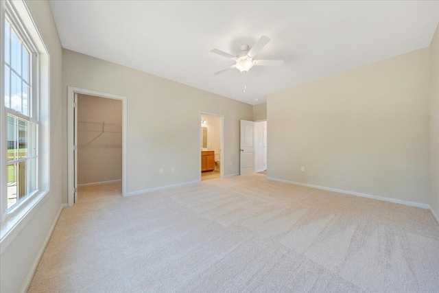 unfurnished bedroom with light carpet, ensuite bath, ceiling fan, a spacious closet, and a closet