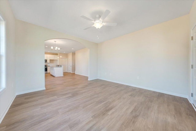 unfurnished living room featuring ceiling fan with notable chandelier and light hardwood / wood-style flooring