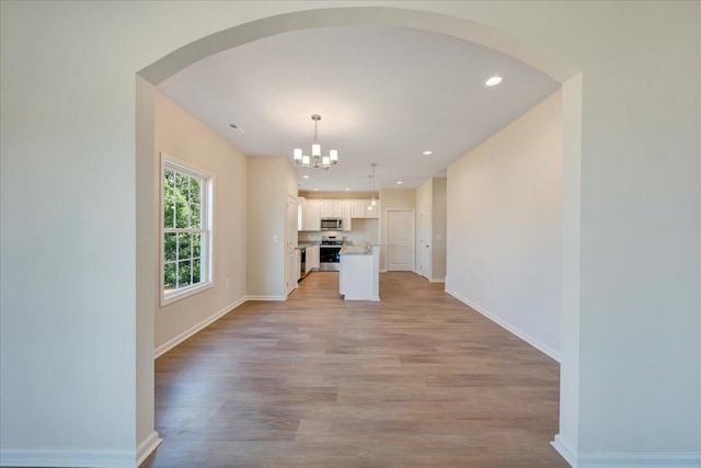 unfurnished living room with light wood-type flooring and an inviting chandelier