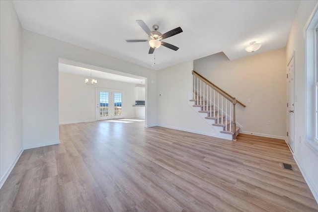 unfurnished living room featuring french doors, ceiling fan with notable chandelier, and light hardwood / wood-style flooring