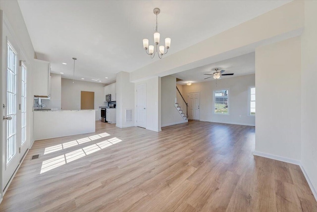 unfurnished living room with ceiling fan with notable chandelier and light hardwood / wood-style floors