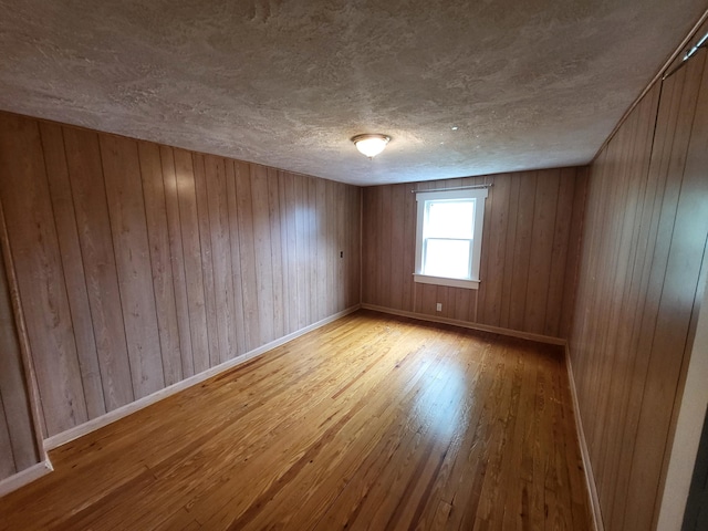 unfurnished room with light wood-type flooring, a textured ceiling, and wooden walls