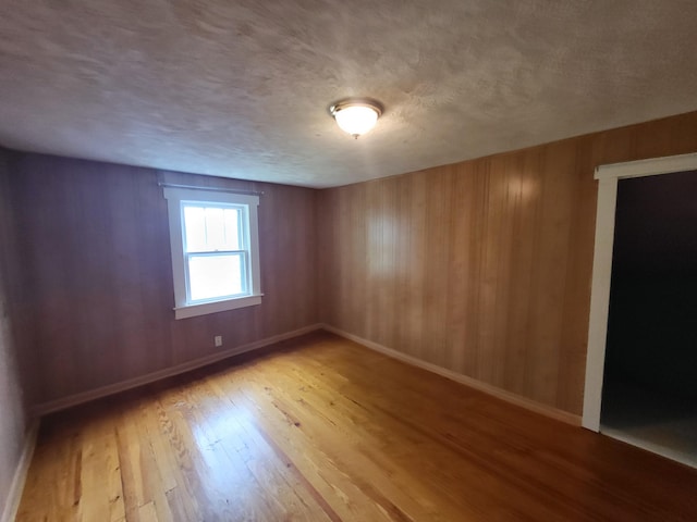 spare room featuring wood walls, light hardwood / wood-style flooring, and a textured ceiling