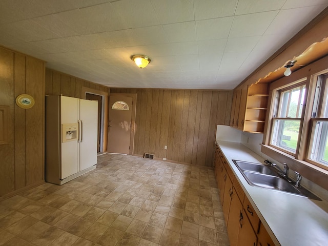 kitchen with white refrigerator with ice dispenser, sink, and wooden walls