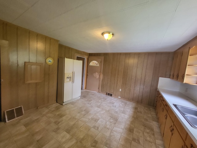 interior space with wood walls, white refrigerator with ice dispenser, and sink