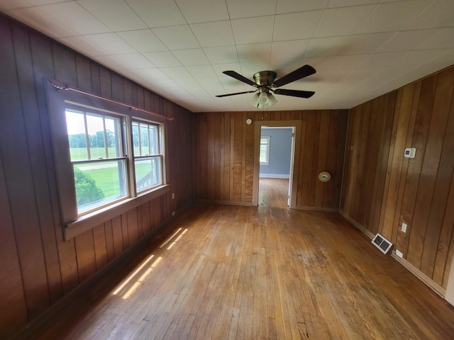 empty room featuring ceiling fan, wooden walls, and light hardwood / wood-style floors