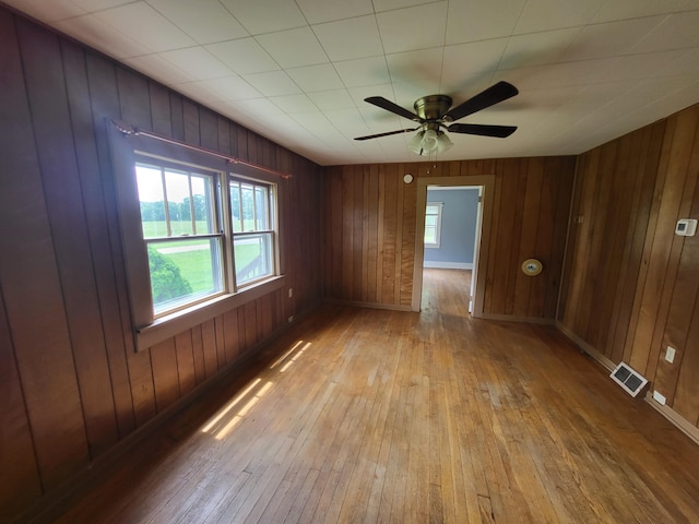 spare room featuring light hardwood / wood-style flooring, ceiling fan, and wood walls