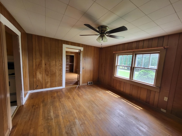 spare room with ceiling fan, light hardwood / wood-style floors, and wood walls