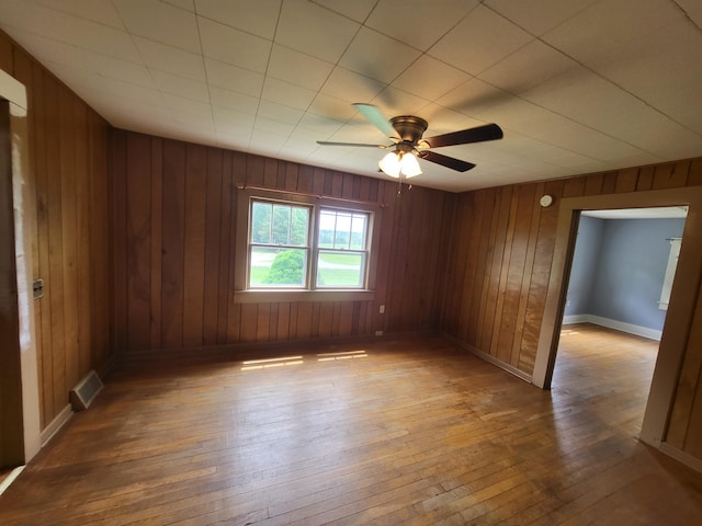 empty room featuring hardwood / wood-style floors, ceiling fan, and wood walls