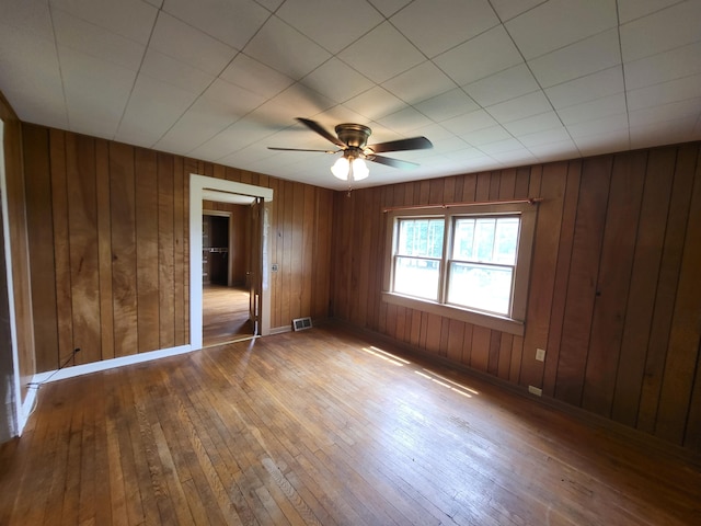 unfurnished bedroom featuring hardwood / wood-style flooring, ceiling fan, and wood walls