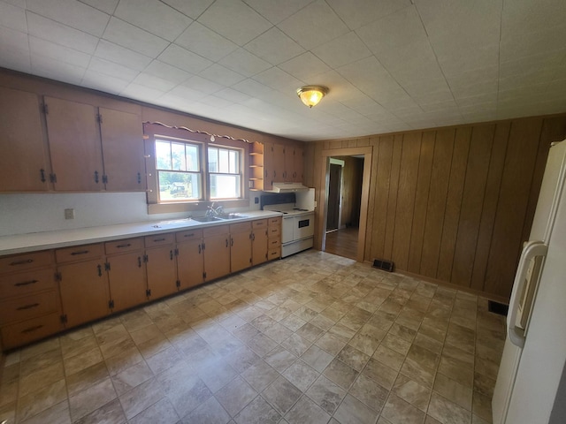 kitchen with sink, range, white refrigerator, and wood walls