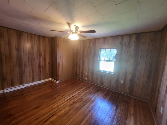 spare room with wood walls, dark hardwood / wood-style floors, ceiling fan, and a baseboard heating unit