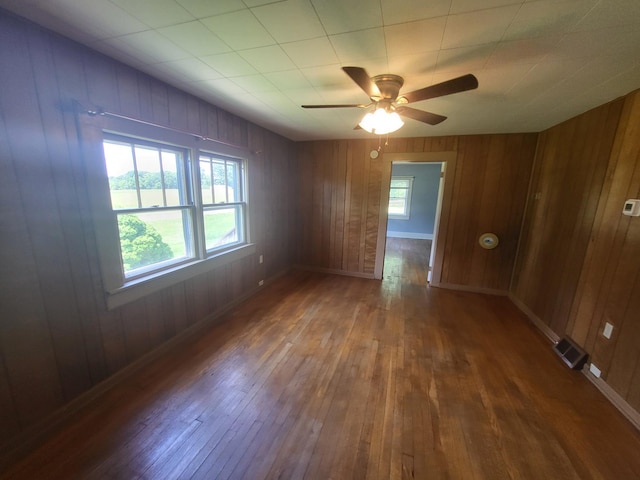 unfurnished room with wooden walls, ceiling fan, and dark wood-type flooring