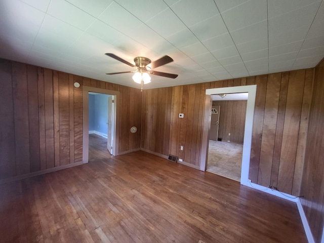 empty room with wooden walls, ceiling fan, and hardwood / wood-style flooring