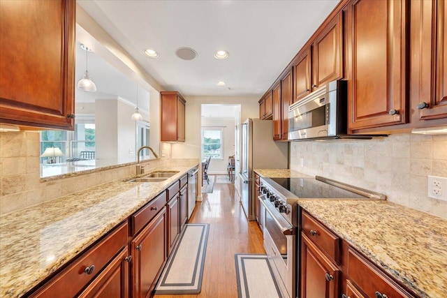 kitchen with sink, stainless steel appliances, light stone counters, and hanging light fixtures