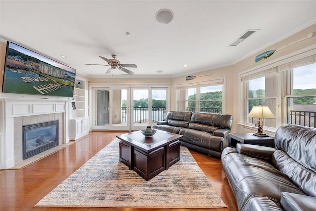 living room with a fireplace, ceiling fan, crown molding, and light wood-type flooring