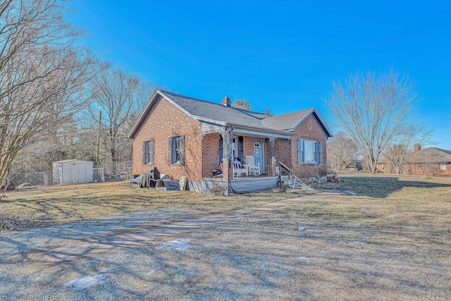 view of front facade with covered porch, a front yard, and a shed