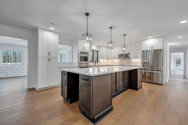 kitchen featuring appliances with stainless steel finishes, hanging light fixtures, a center island, light hardwood / wood-style floors, and white cabinets